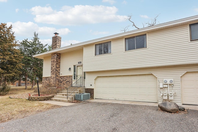 split foyer home with central AC unit, a chimney, driveway, a garage, and brick siding