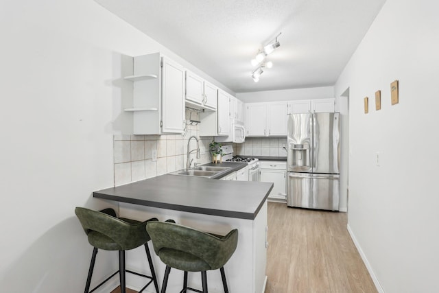 kitchen featuring open shelves, backsplash, a sink, white appliances, and a peninsula