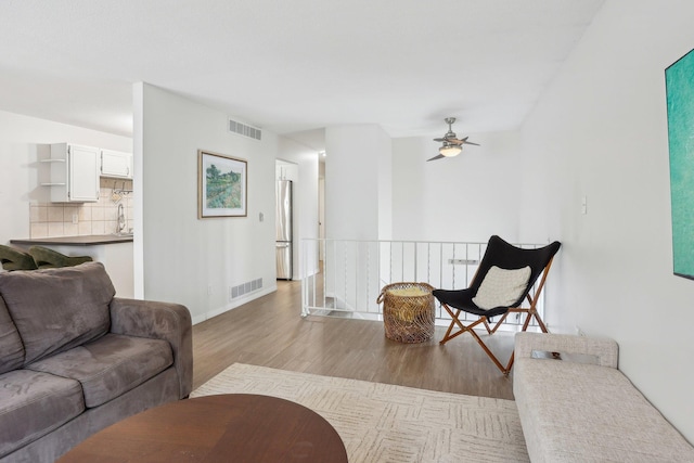 living room with wood finished floors, visible vents, a ceiling fan, and baseboards