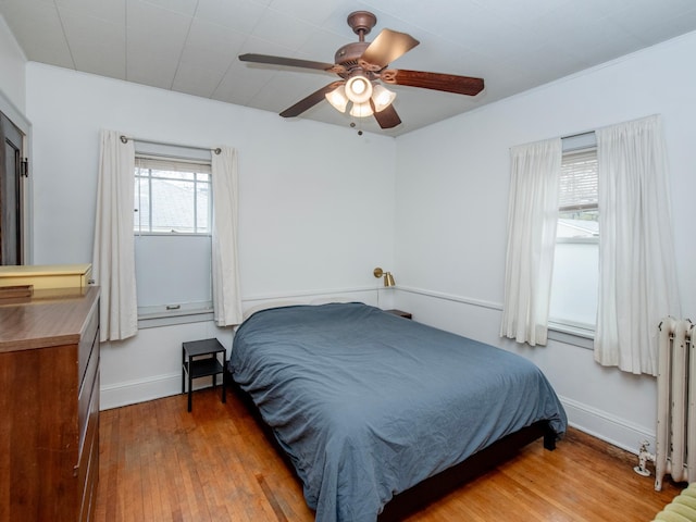 bedroom with baseboards, a ceiling fan, radiator, and wood finished floors