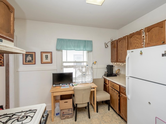 kitchen with light countertops, freestanding refrigerator, brown cabinets, and gas range oven