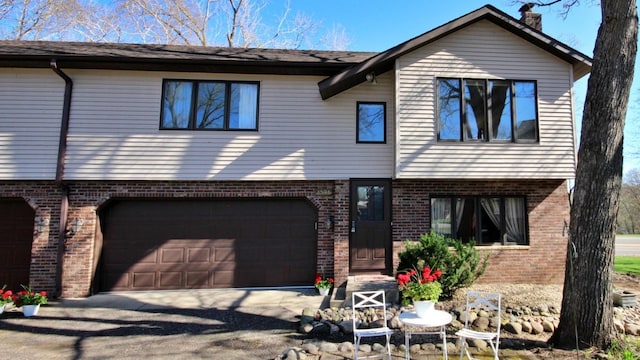 view of front facade featuring brick siding, an attached garage, driveway, and a chimney