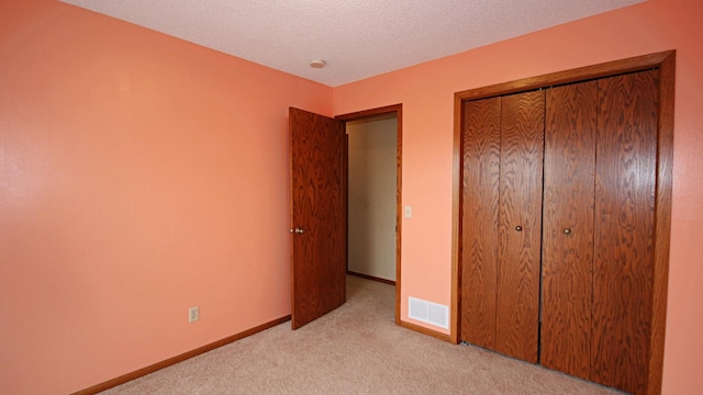 unfurnished bedroom featuring visible vents, a closet, baseboards, light colored carpet, and a textured ceiling