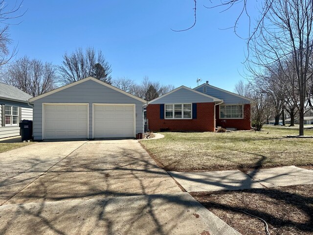single story home featuring a detached garage, a front yard, brick siding, and an outbuilding