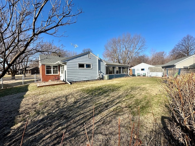 rear view of property with a fenced backyard, brick siding, a wooden deck, a sunroom, and a lawn