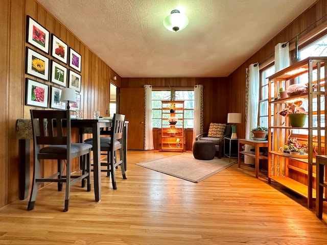 sitting room with wooden walls, a textured ceiling, and light wood finished floors