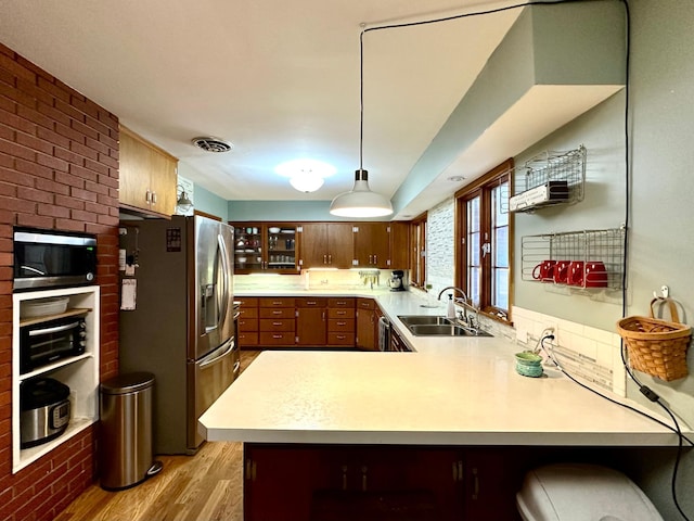 kitchen featuring appliances with stainless steel finishes, light countertops, light wood finished floors, a sink, and a peninsula