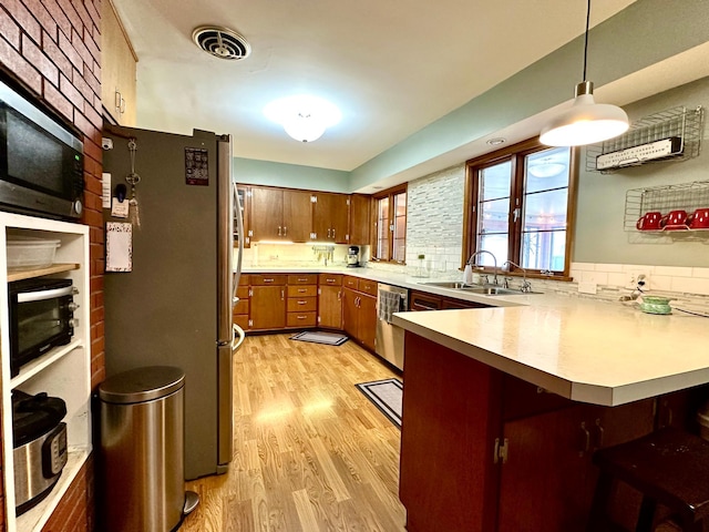 kitchen featuring light wood finished floors, a sink, stainless steel appliances, a peninsula, and light countertops