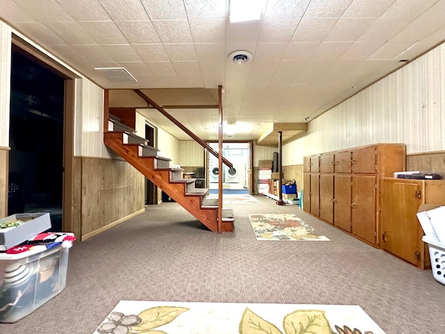finished basement featuring wood walls, carpet, visible vents, and stairway