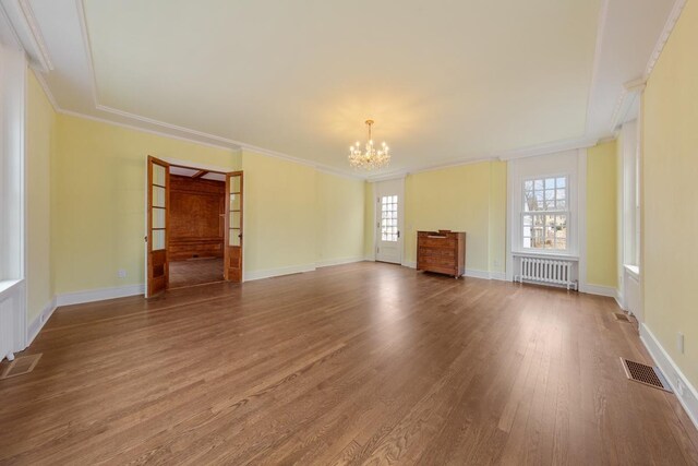 525 Main St, Owatonna, MN 55060 - unfurnished living room featuring radiator heating unit, ornamental molding, visible vents, a chandelier, and wood finished floors