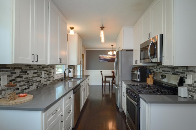 kitchen with appliances with stainless steel finishes, a sink, white cabinets, dark wood finished floors, and a wainscoted wall