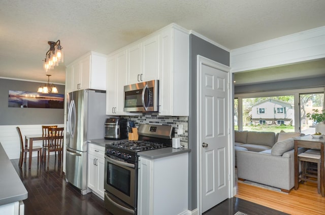 kitchen with appliances with stainless steel finishes, a chandelier, ornamental molding, white cabinets, and dark wood-type flooring