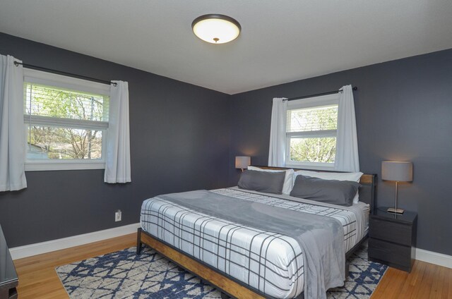 bedroom with multiple windows, wood finished floors, and baseboards