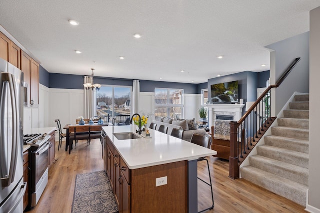 6921 Huckleberry Dr, Minnetrista, MN 55331 - kitchen with appliances with stainless steel finishes, brown cabinetry, a fireplace, a kitchen bar, and a kitchen island with sink
