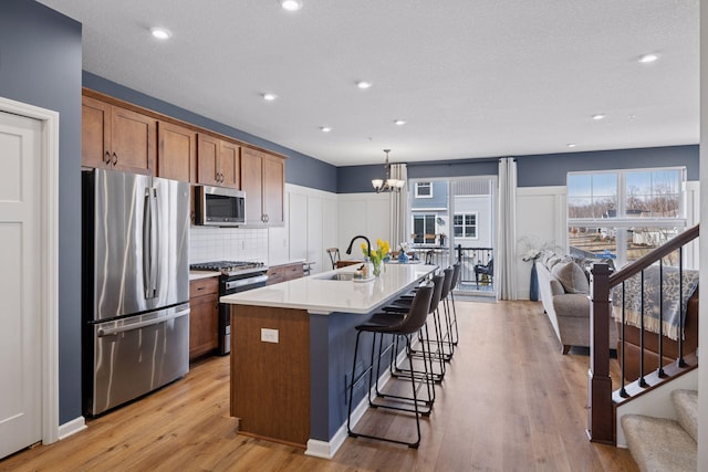 6921 Huckleberry Dr, Minnetrista, MN 55331 - kitchen featuring appliances with stainless steel finishes, brown cabinets, a chandelier, a center island with sink, and a kitchen bar