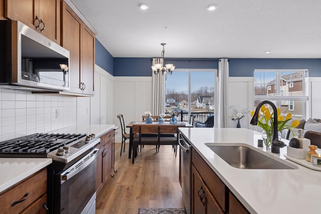 6921 Huckleberry Dr, Minnetrista, MN 55331 - kitchen with stainless steel appliances, light countertops, light wood-type flooring, a chandelier, and tasteful backsplash