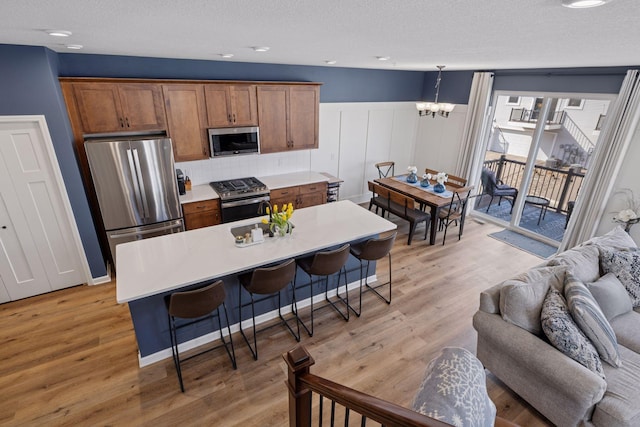 6921 Huckleberry Dr, Minnetrista, MN 55331 - kitchen featuring stainless steel appliances, a chandelier, a breakfast bar area, light wood-style flooring, and brown cabinetry