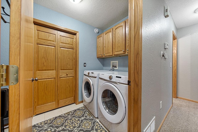 washroom featuring washer and clothes dryer, cabinet space, a textured ceiling, and visible vents