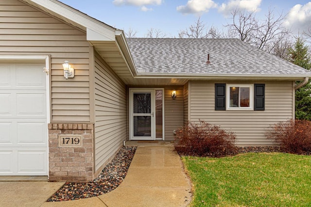 view of exterior entry with a garage, a yard, and roof with shingles