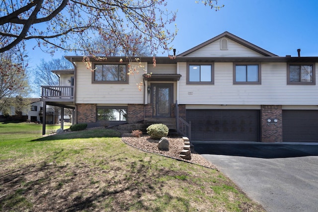 raised ranch with a garage, driveway, a front lawn, and brick siding