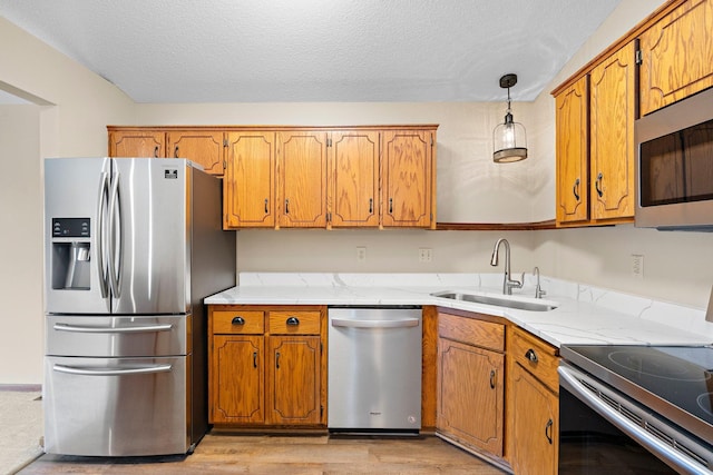kitchen featuring brown cabinets, appliances with stainless steel finishes, a sink, light wood-style floors, and light countertops