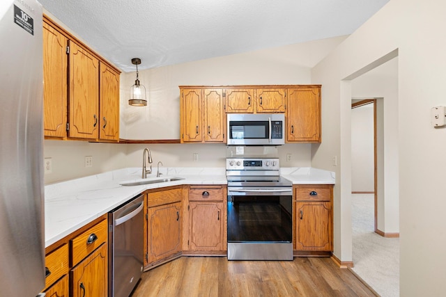 kitchen featuring a sink, light wood finished floors, brown cabinetry, stainless steel appliances, and vaulted ceiling