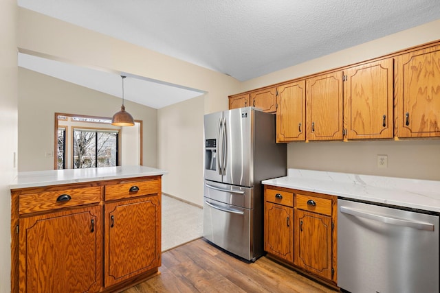 kitchen featuring brown cabinets, light countertops, stainless steel appliances, wood finished floors, and lofted ceiling