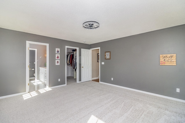 unfurnished bedroom with a walk in closet, ensuite bath, carpet floors, baseboards, and a closet