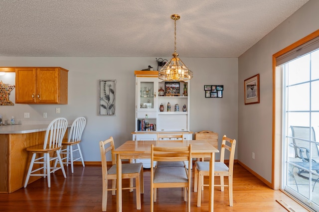 dining room with light wood finished floors, a textured ceiling, baseboards, and an inviting chandelier
