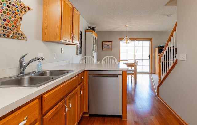 kitchen with stainless steel dishwasher, dark wood finished floors, a sink, a peninsula, and light countertops