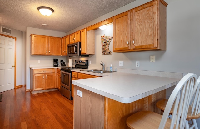 kitchen with a peninsula, a sink, stainless steel appliances, visible vents, and light countertops