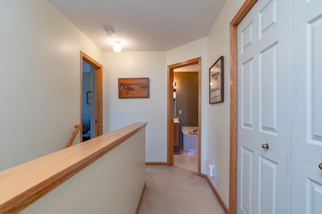 corridor with a textured ceiling, baseboards, an upstairs landing, and light colored carpet