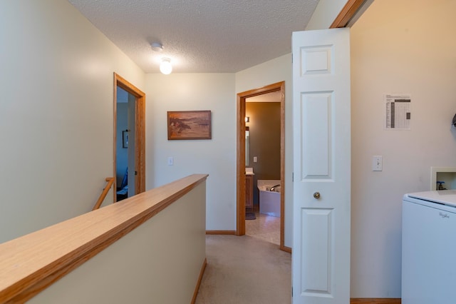 corridor with an upstairs landing, a textured ceiling, baseboards, light carpet, and washer / clothes dryer