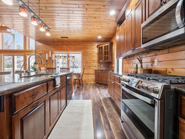 kitchen featuring wood walls, stainless steel appliances, wooden ceiling, a sink, and dark stone counters