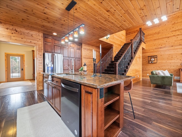 kitchen featuring dark wood finished floors, wooden walls, dishwashing machine, stainless steel fridge, and brown cabinetry