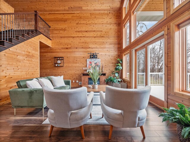 living area with wood finished floors, wooden walls, a towering ceiling, and stairs