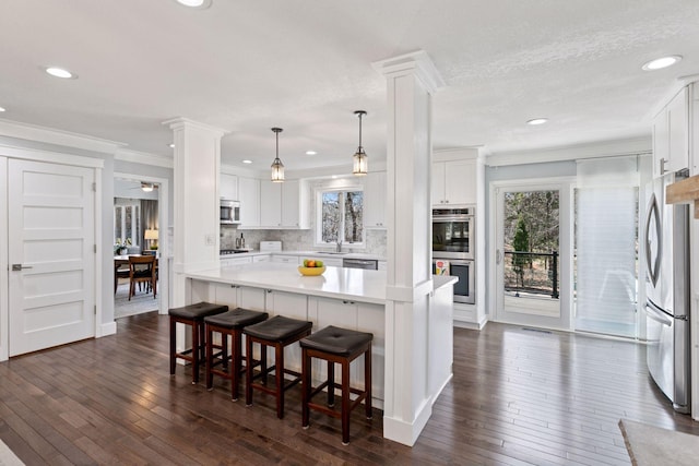 kitchen with white cabinets, dark wood finished floors, light countertops, decorative columns, and appliances with stainless steel finishes