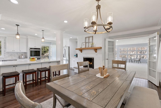 dining space with dark wood finished floors, recessed lighting, a chandelier, crown molding, and a fireplace