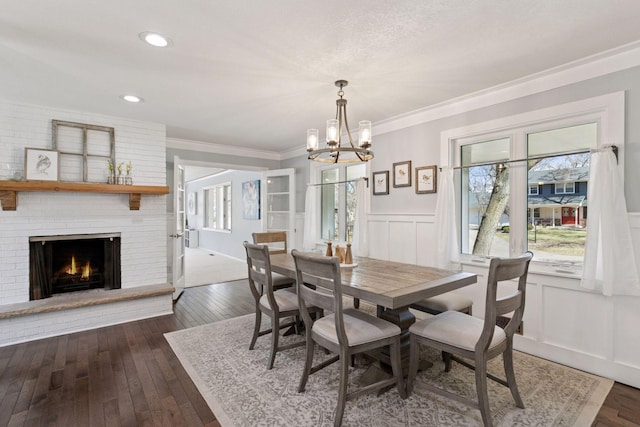 dining room with a brick fireplace, dark wood-style flooring, a notable chandelier, and wainscoting