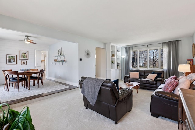living area with light colored carpet, ceiling fan, and baseboards