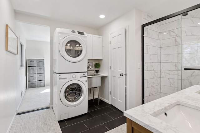 washroom with baseboards, cabinet space, stacked washer / dryer, and a sink