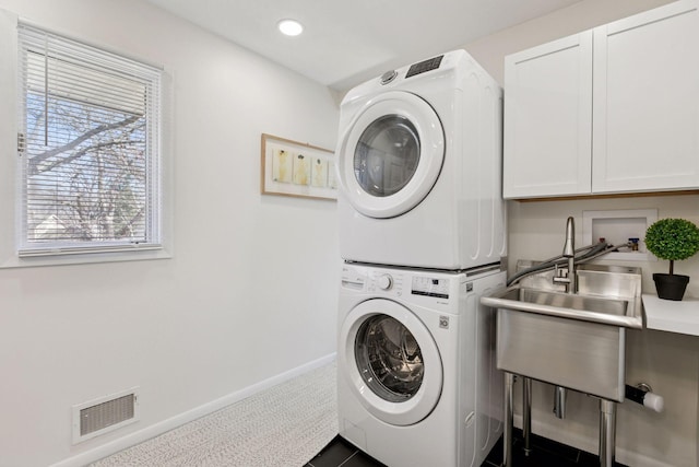 laundry room featuring baseboards, visible vents, recessed lighting, cabinet space, and stacked washing maching and dryer