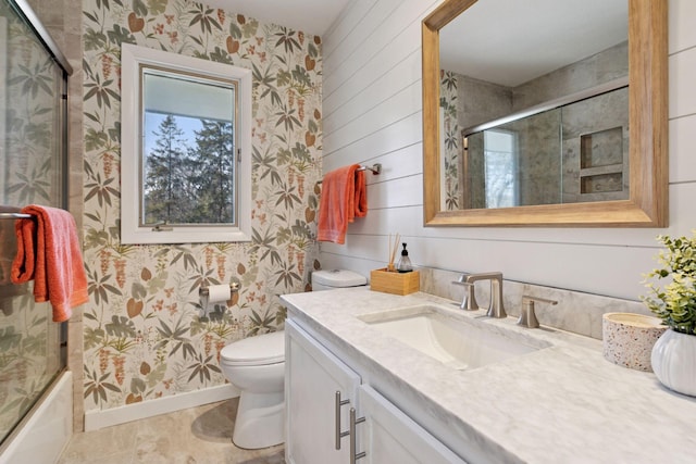 bathroom featuring wallpapered walls, enclosed tub / shower combo, toilet, vanity, and baseboards