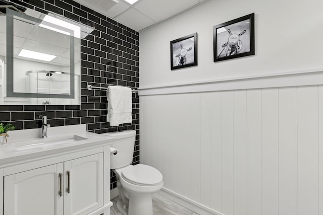 bathroom featuring a wainscoted wall, toilet, tile walls, marble finish floor, and vanity
