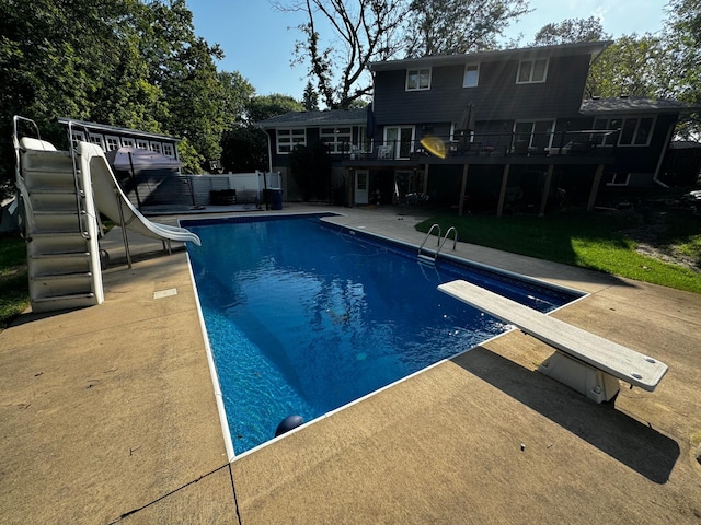 pool with a deck, a water slide, a patio, and a diving board