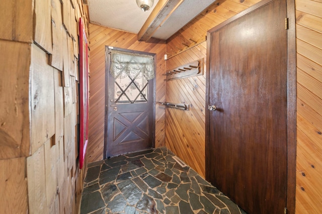 doorway featuring stone flooring, beam ceiling, and wood walls