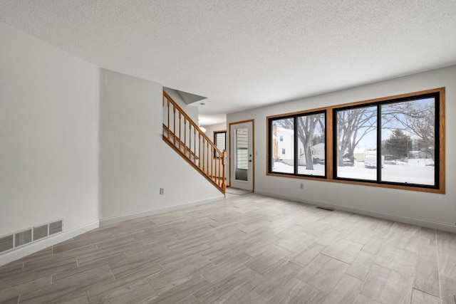unfurnished living room with light wood finished floors, baseboards, visible vents, and stairway