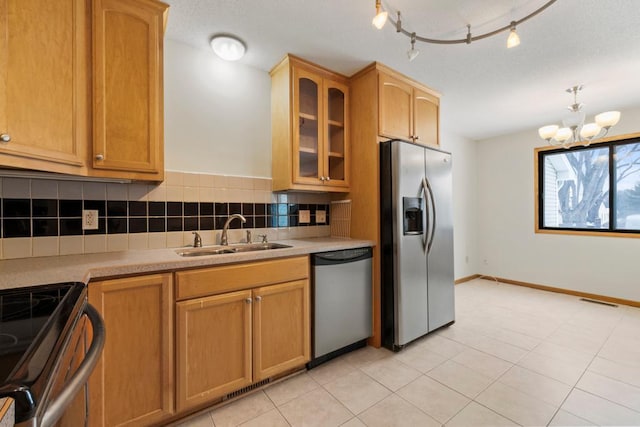 kitchen with an inviting chandelier, glass insert cabinets, tasteful backsplash, appliances with stainless steel finishes, and a sink