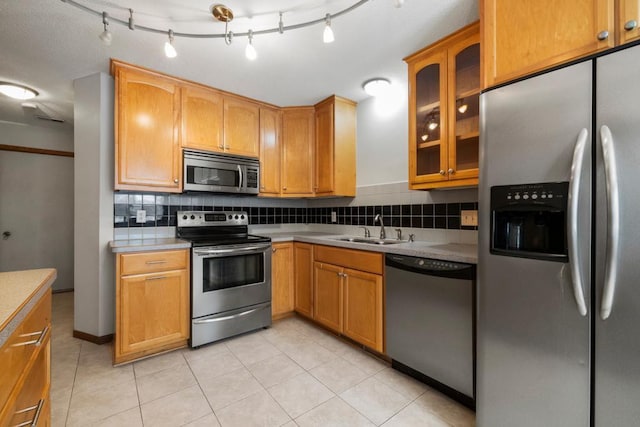 kitchen with glass insert cabinets, appliances with stainless steel finishes, light countertops, a sink, and backsplash