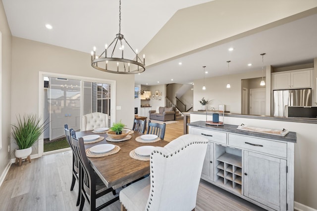 dining area featuring lofted ceiling, stairway, light wood finished floors, a chandelier, and baseboards